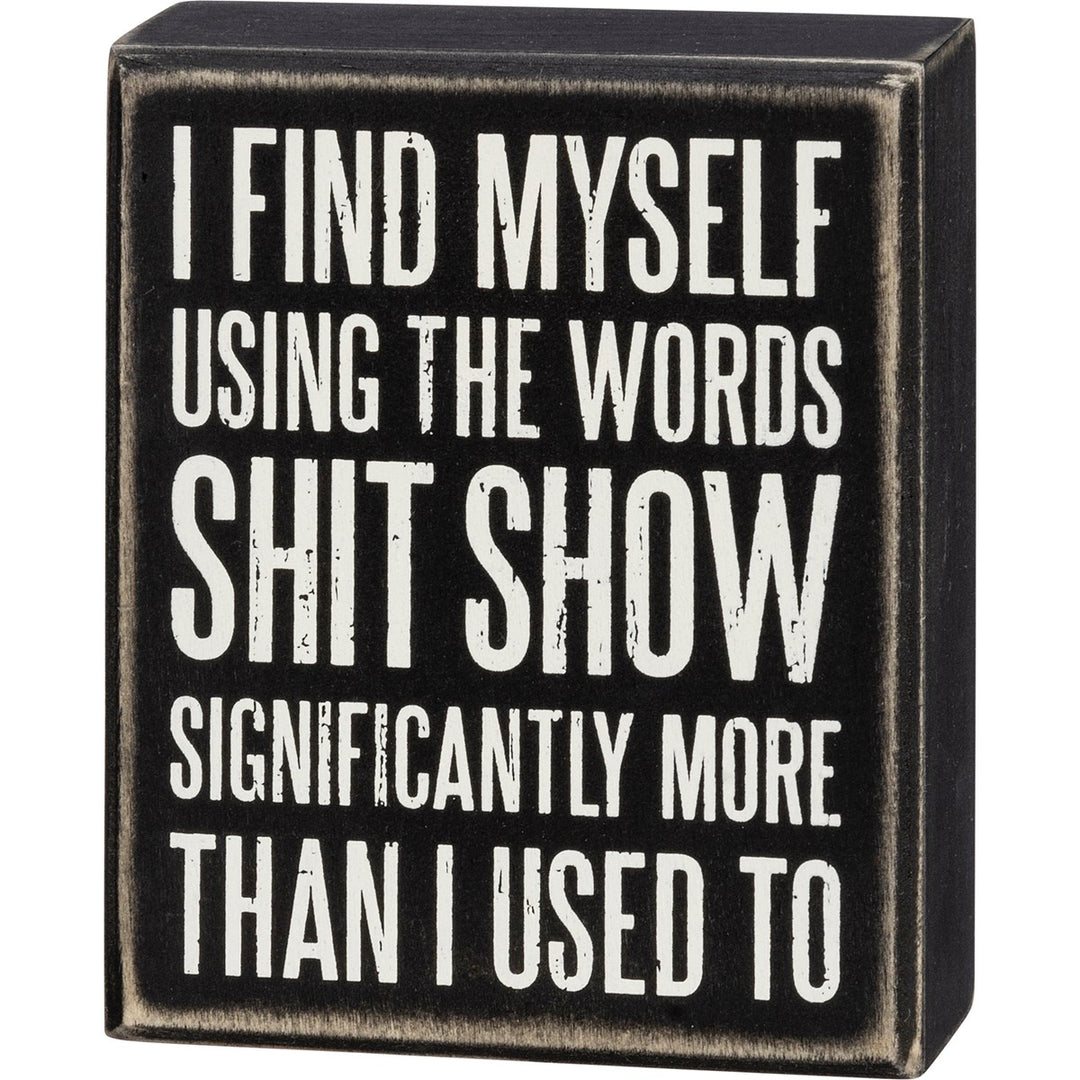 Black wooden box sign with white text that reads 'I FIND MYSELF USING THE WORDS SHIT SHOW SIGNIFICANTLY MORE THAN I USED TO'.