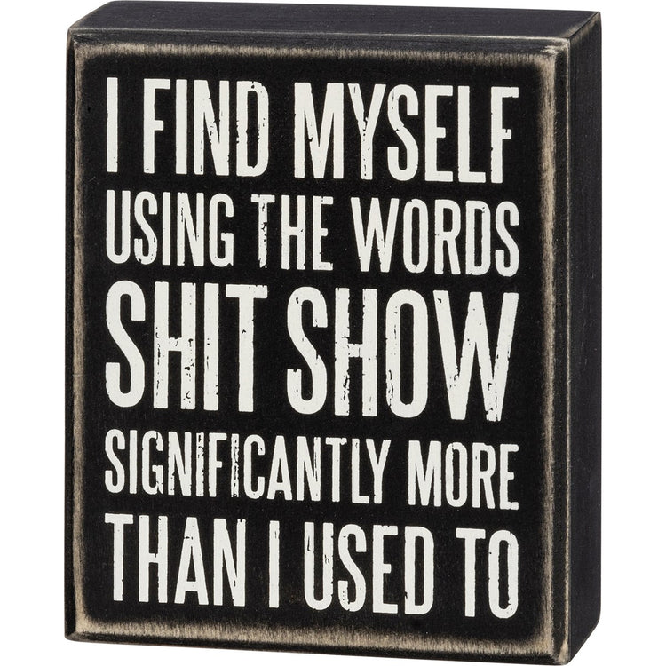 Black wooden box sign with white text that reads 'I FIND MYSELF USING THE WORDS SHIT SHOW SIGNIFICANTLY MORE THAN I USED TO'.
