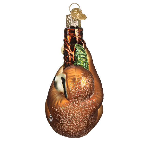 Glass sloth Christmas ornament hanging from a brown branch with green glitter leaves.