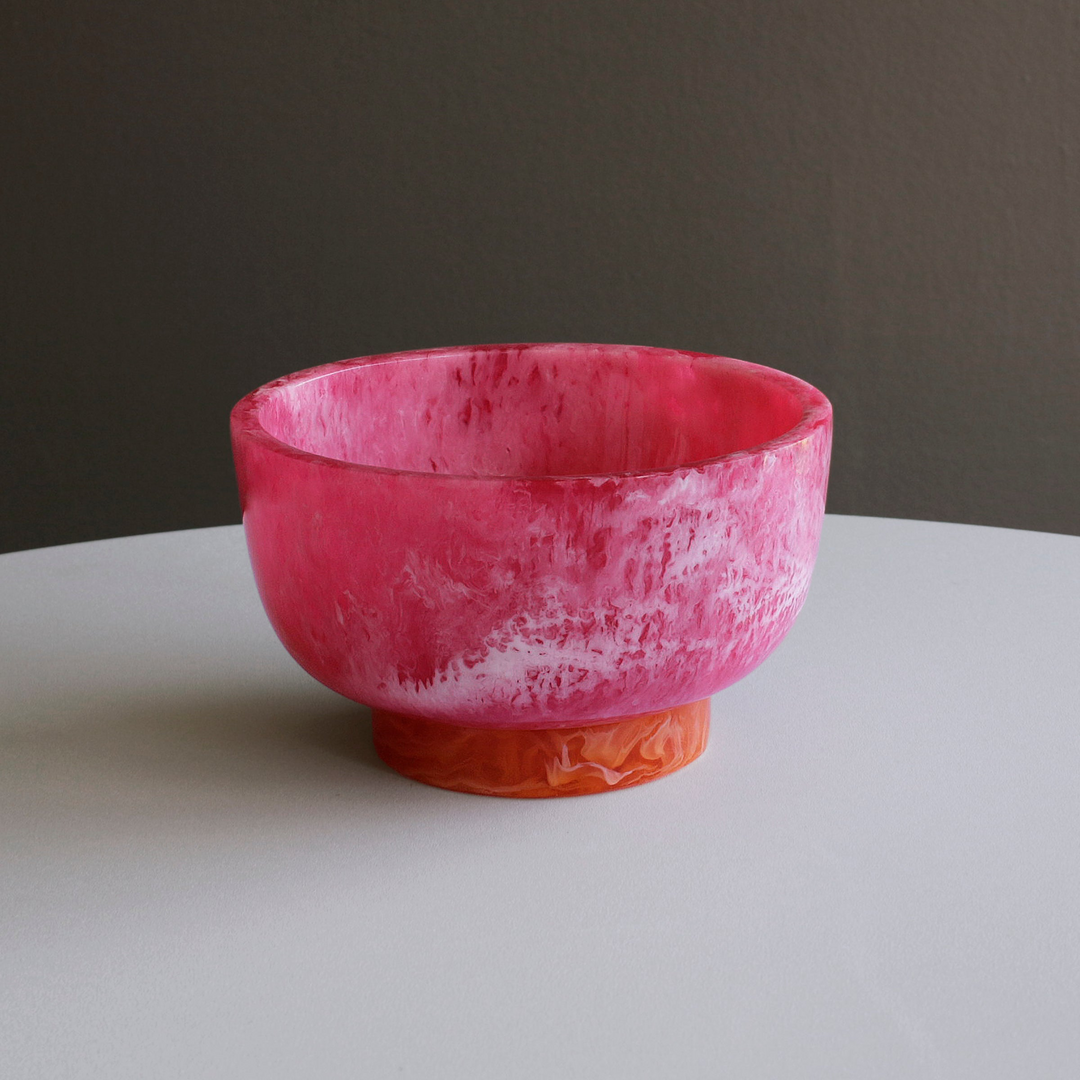 Pink marbled resin bowl with a contrasting orange base on a white surface.