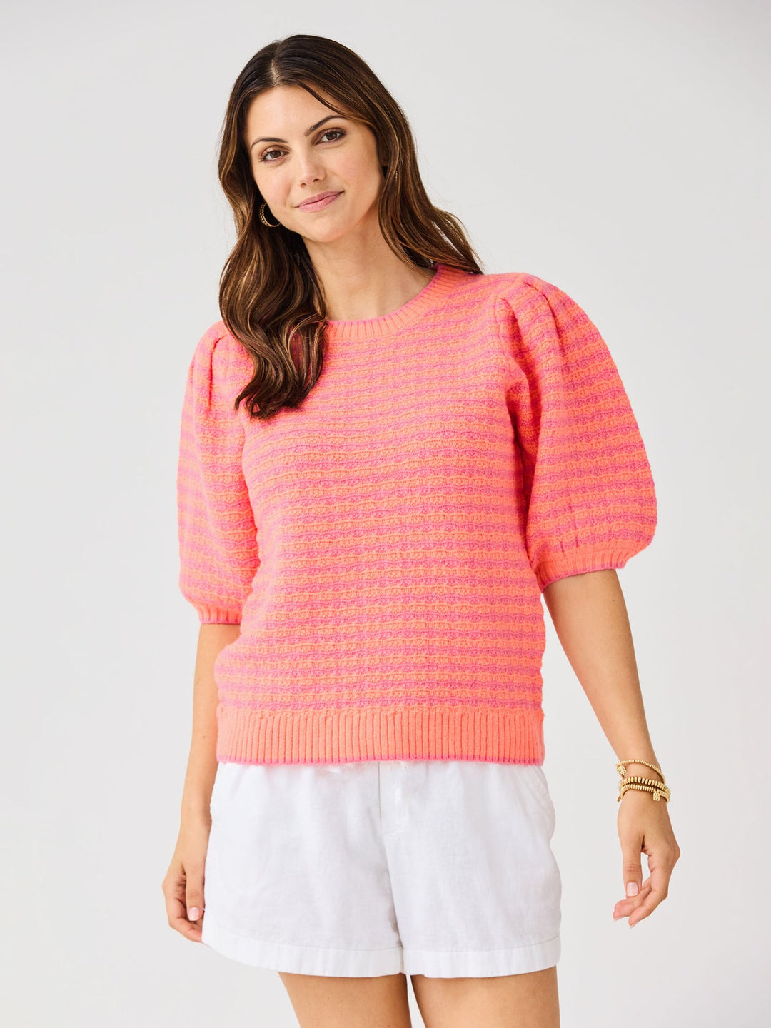 Woman wearing the Abigail Sweater, a pink and orange striped knit top with puff sleeves.