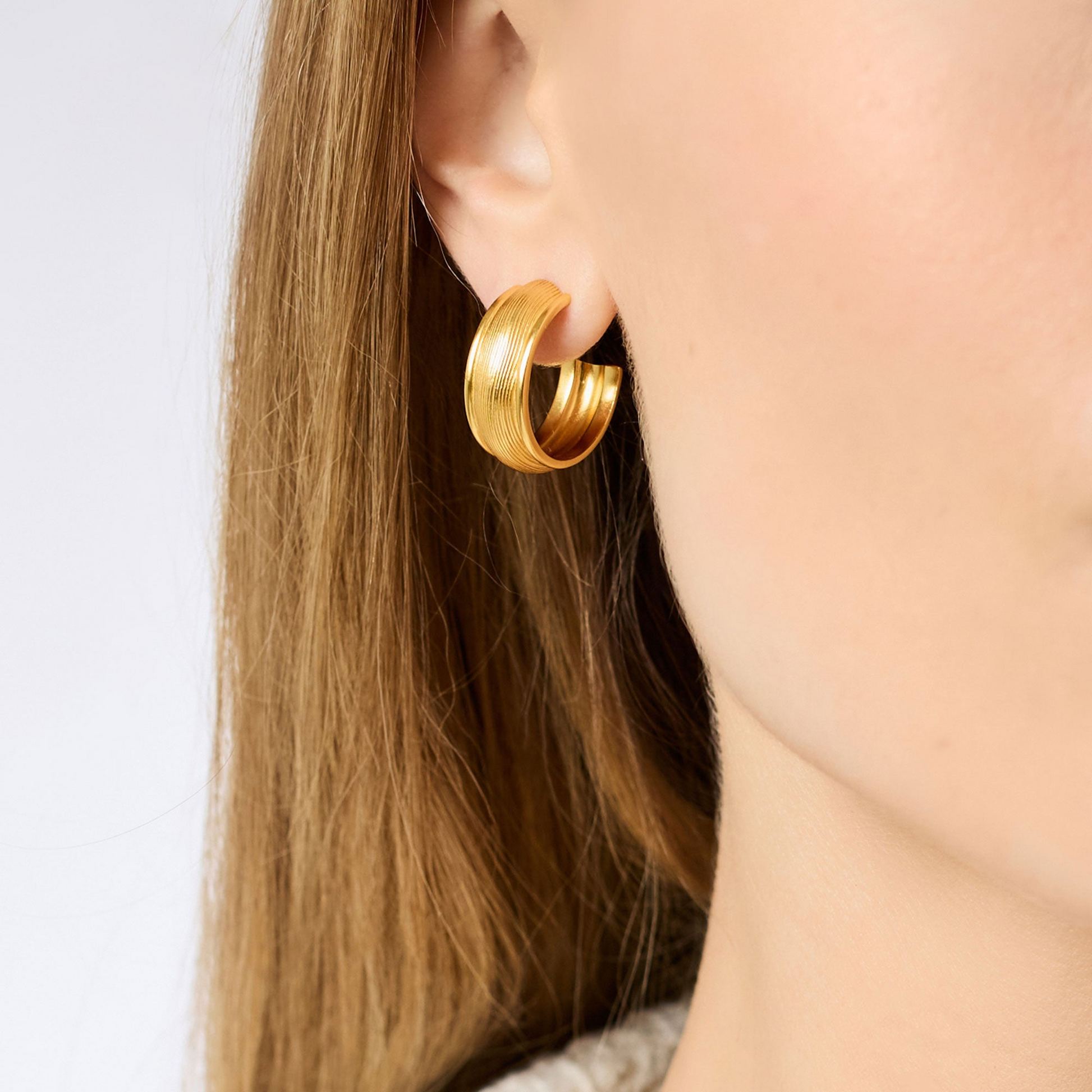 Close-up of a person wearing a 24K gold plated Cobblestone Hoop earring with textured detailing.