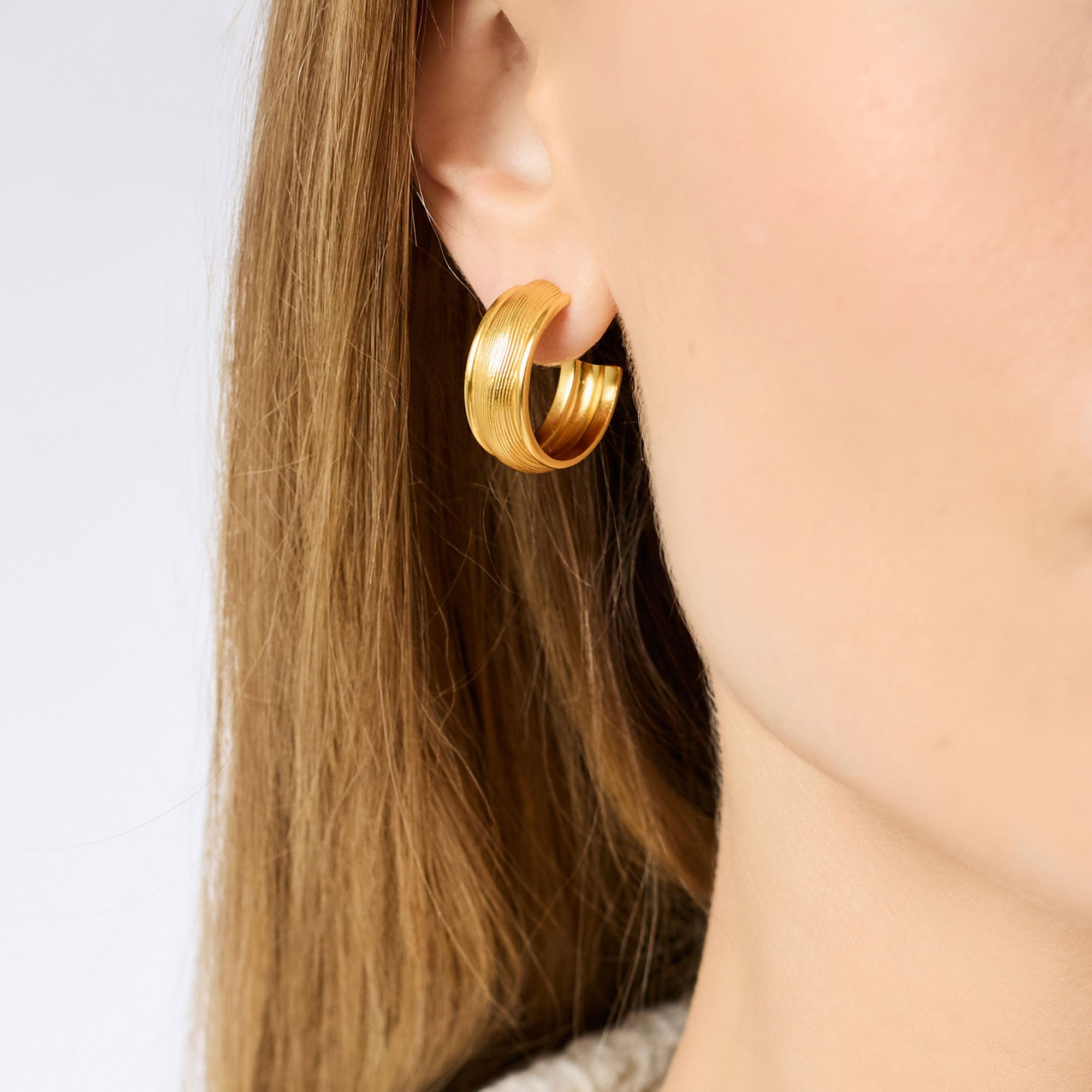 Close-up of a person wearing a 24K gold plated Cobblestone Hoop earring with textured detailing.