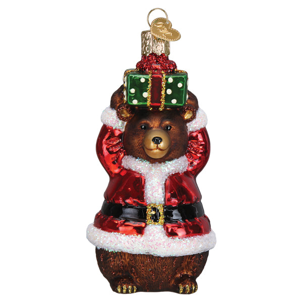 Glass Christmas bear ornament wearing a Santa suit and holding a green gift box on its head.
