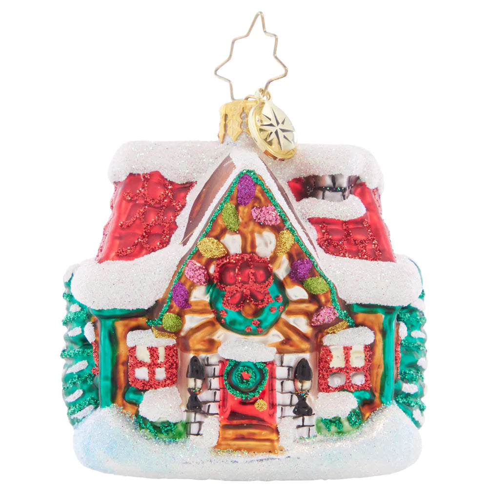 Glass Christmas ornament of a cozy cottage with red roof, glittery snow, and festive decorations.