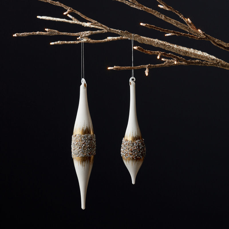 Two white drop glass ornaments with gold and silver glitter accents hanging from a gold branch.