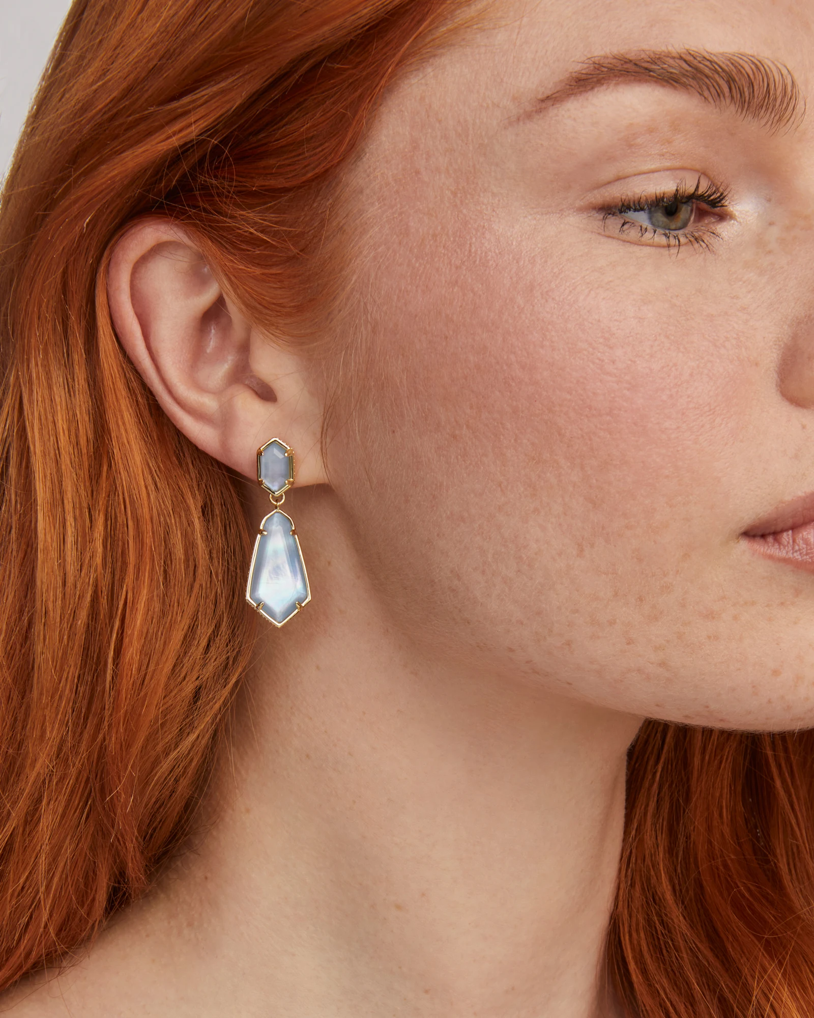 Close-up of a woman wearing Hallie Convertible Drop Earrings with light blue stones in gold frames.