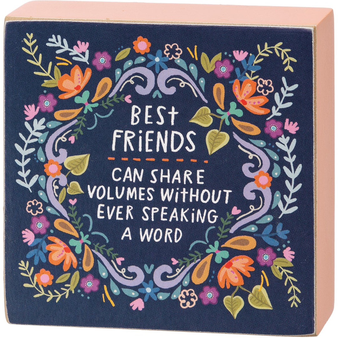 Navy blue wooden box sign with floral wreath and quote 'BEST FRIENDS CAN SHARE VOLUMES WITHOUT EVER SPEAKING A WORD'.