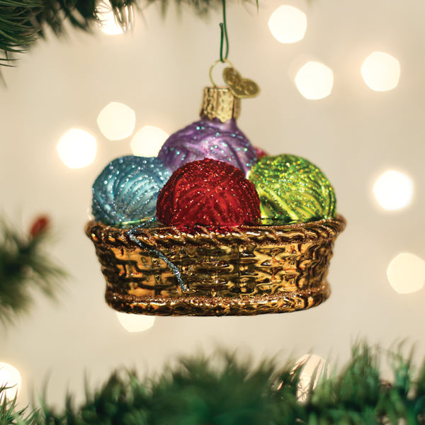 Glass Christmas ornament of a gold basket filled with colorful glittery balls of yarn.
