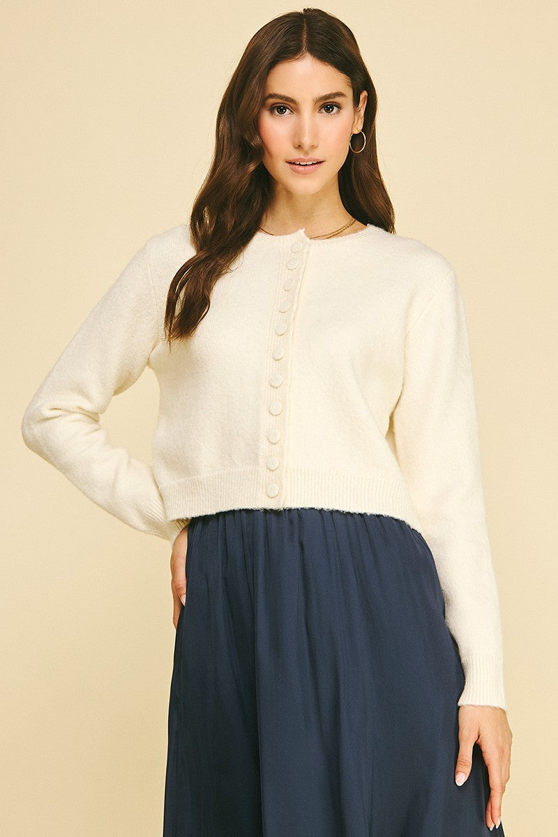 Woman wearing a cream long sleeve cardigan with crystal buttons and a navy blue skirt.