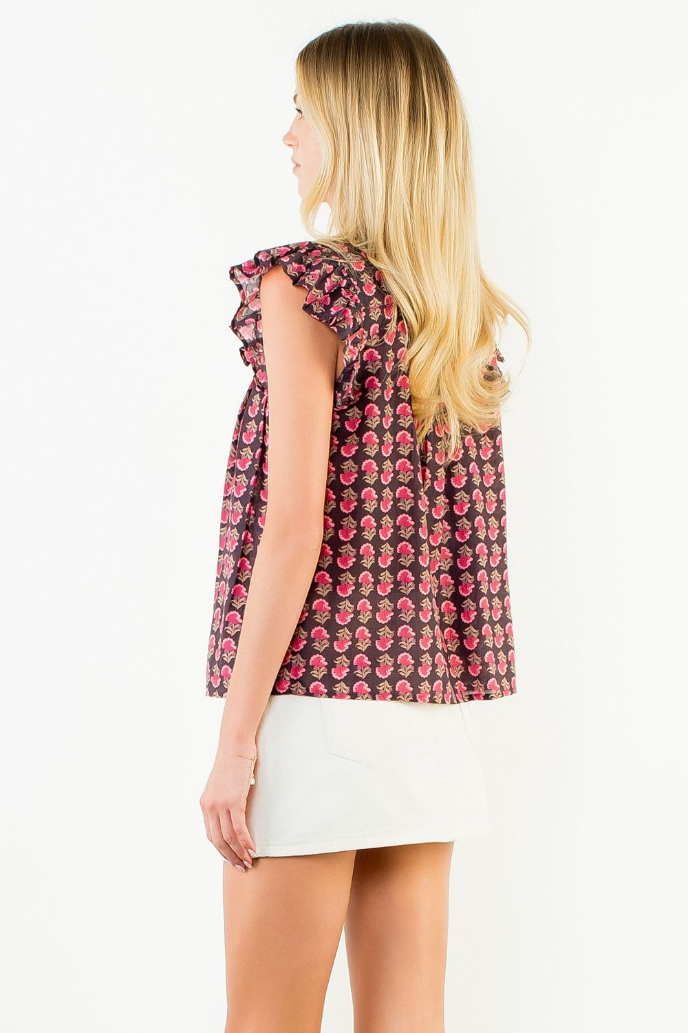 Side view of a woman wearing a dark floral Jane Flutter Sleeve Button Top and white skirt.