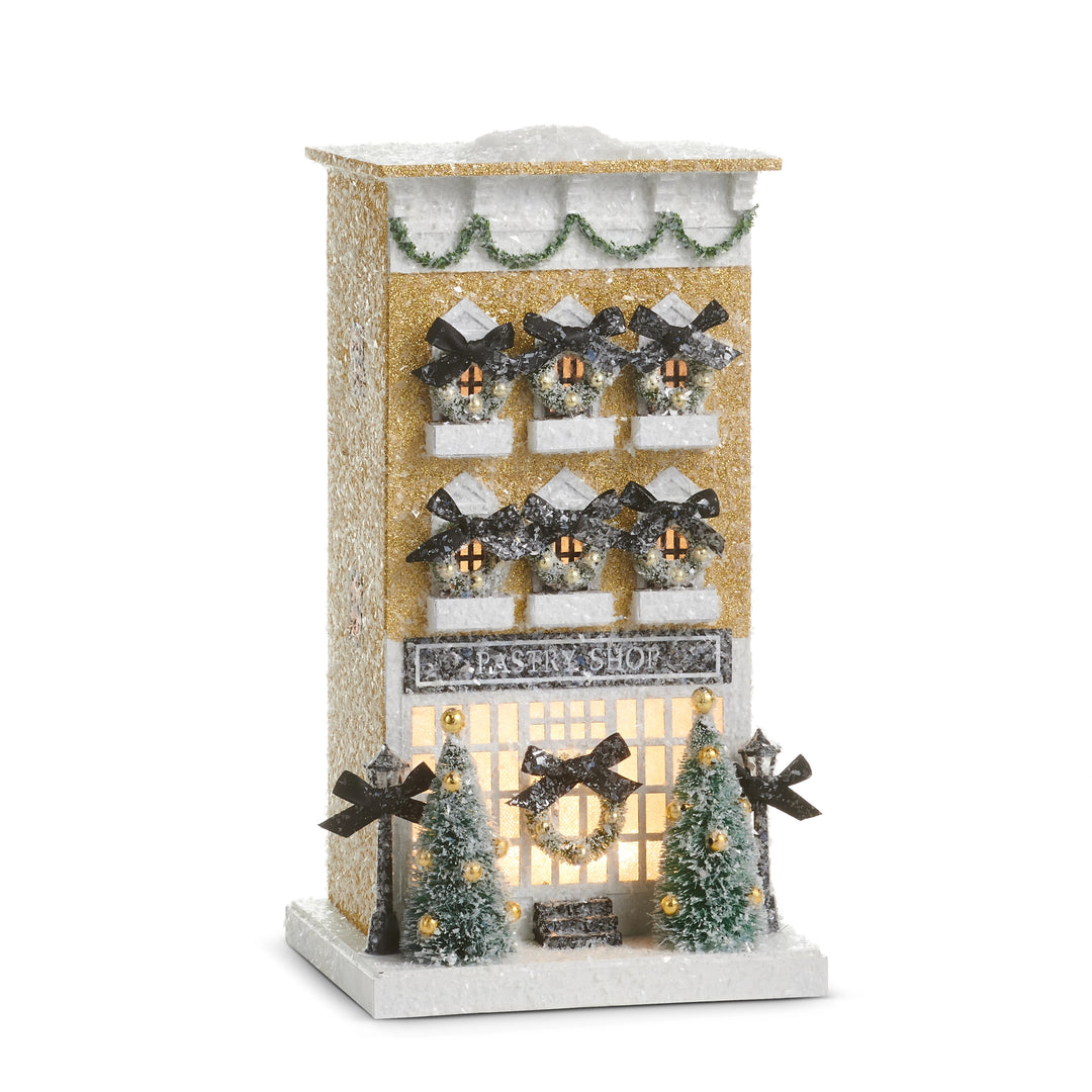 13.25-inch lighted paper pastry shop building with gold glitter, wreaths, and miniature trees.