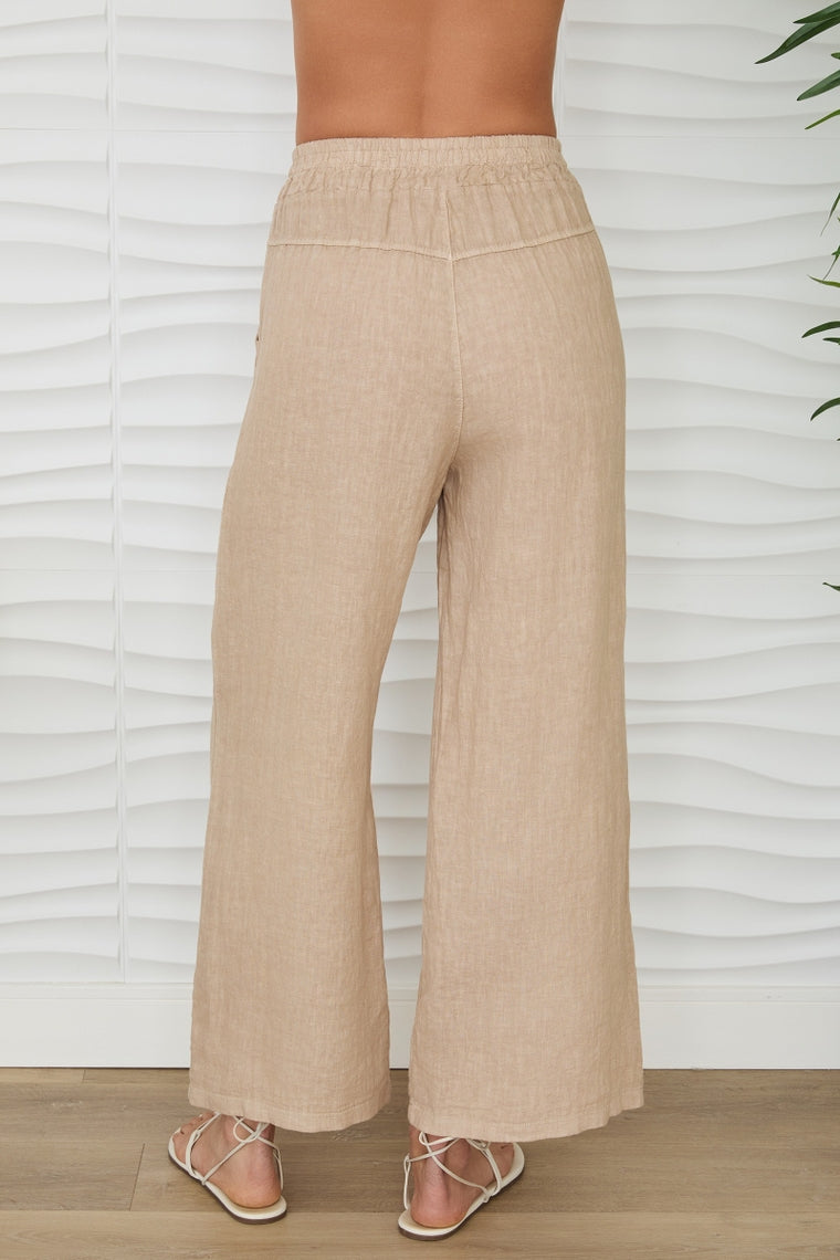 Back view of a person wearing beige linen mid-rise wide-leg pants with an elastic waistband.