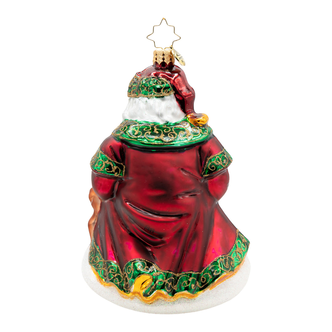 Back view of a Santa glass ornament in a red robe with green and gold glitter trim on snowy base.