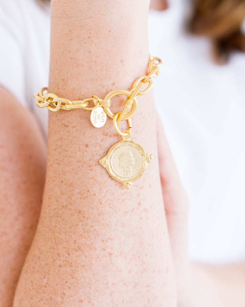 Gold Intaglio Coin Bracelet with a toggle clasp and round coin charm on a person's wrist.