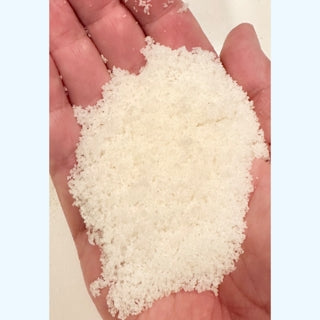 A person holding a handful of white, granular Beach Grass & Dune Bath Salts.