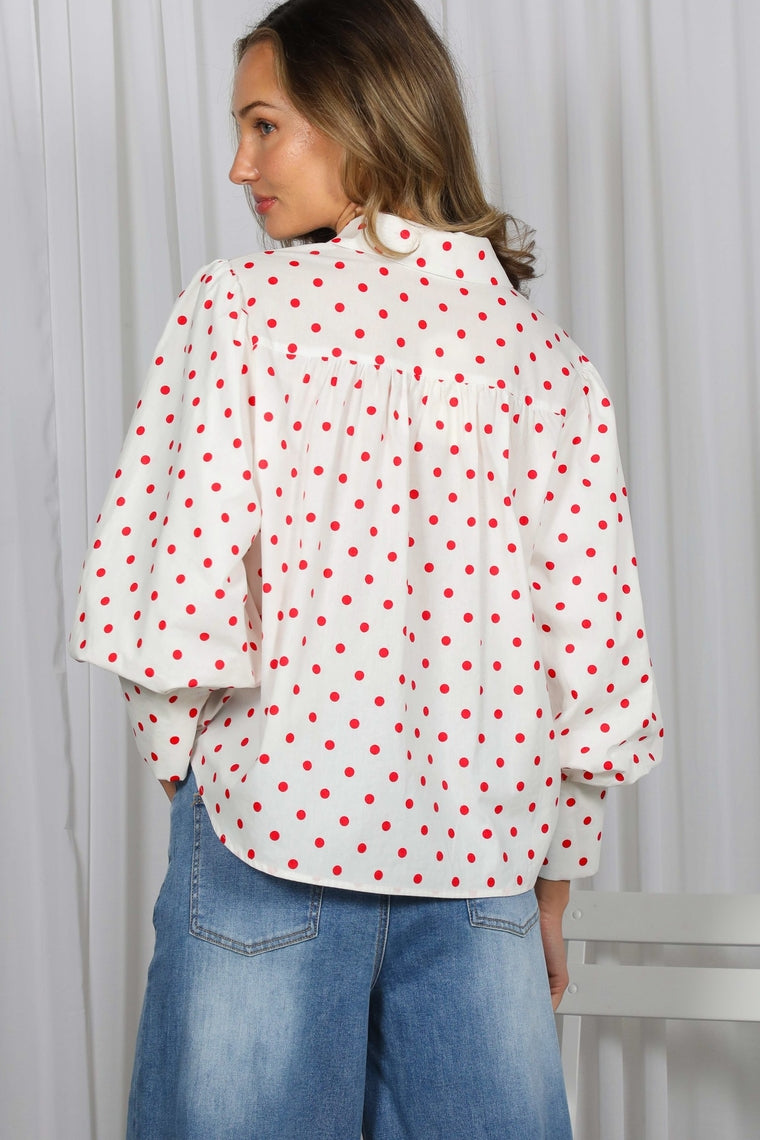 Back view of a woman wearing a white cotton shirt with red polka dots and puff sleeves.