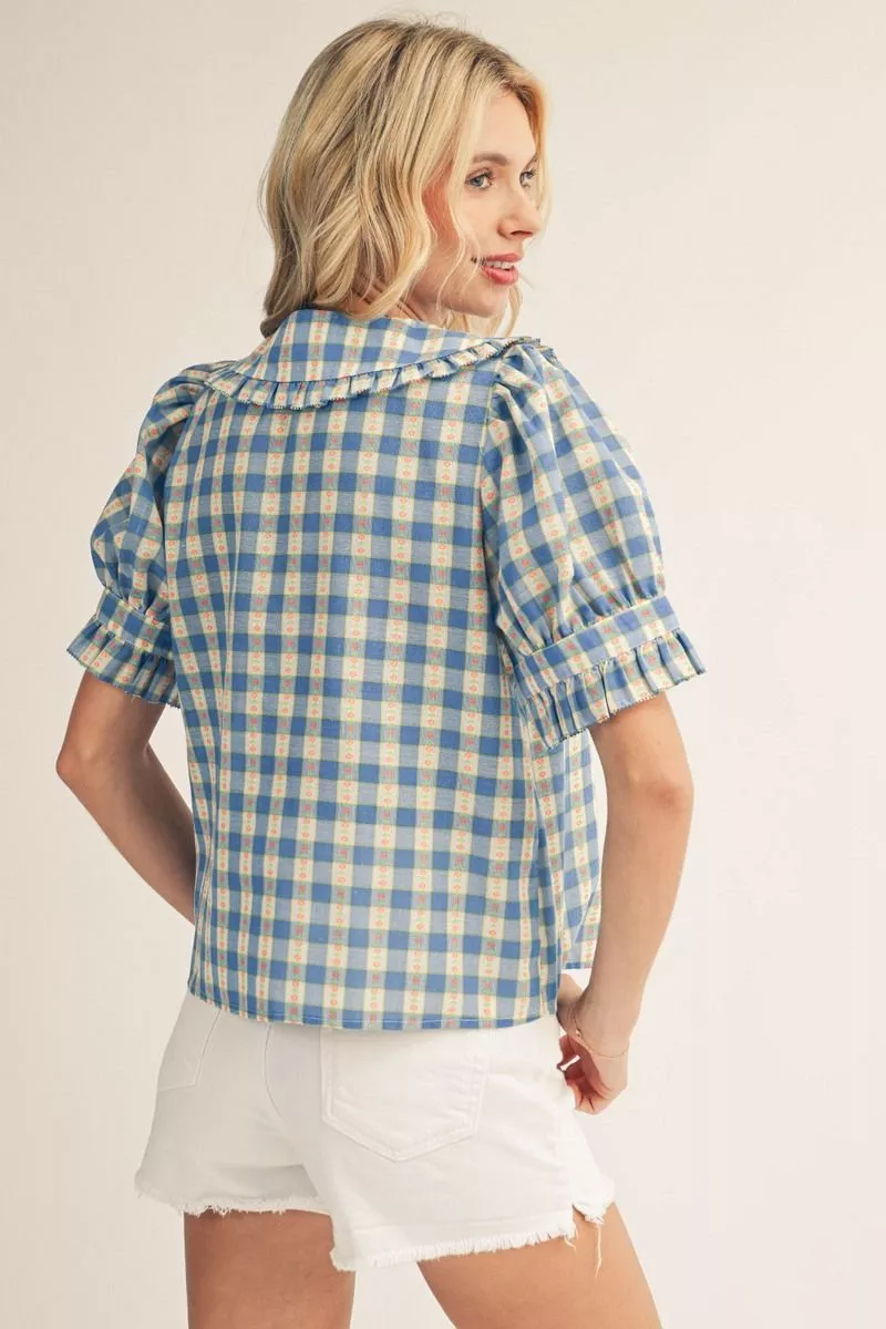 Back view of a woman wearing a blue and yellow check print top with ruffle sleeves and collar.