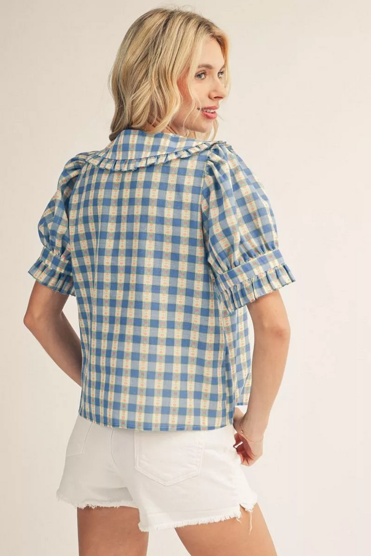 Back view of a woman wearing a blue and yellow check print top with ruffle sleeves and collar.