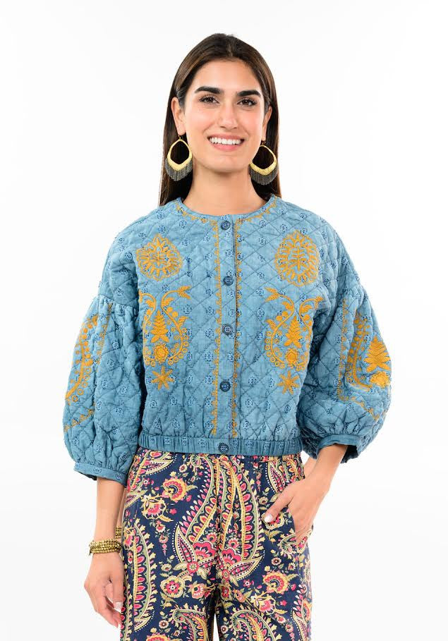 Woman wearing a Jasmin blue quilted jacket with golden floral embroidery and puff sleeves.