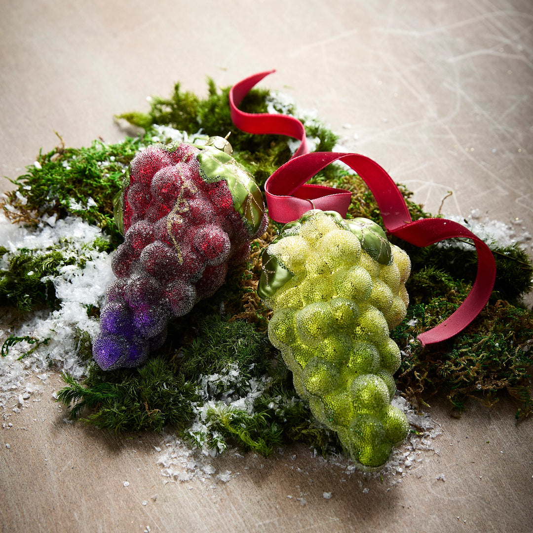 Red and green glittered glass grape cluster ornaments on moss with a red ribbon.