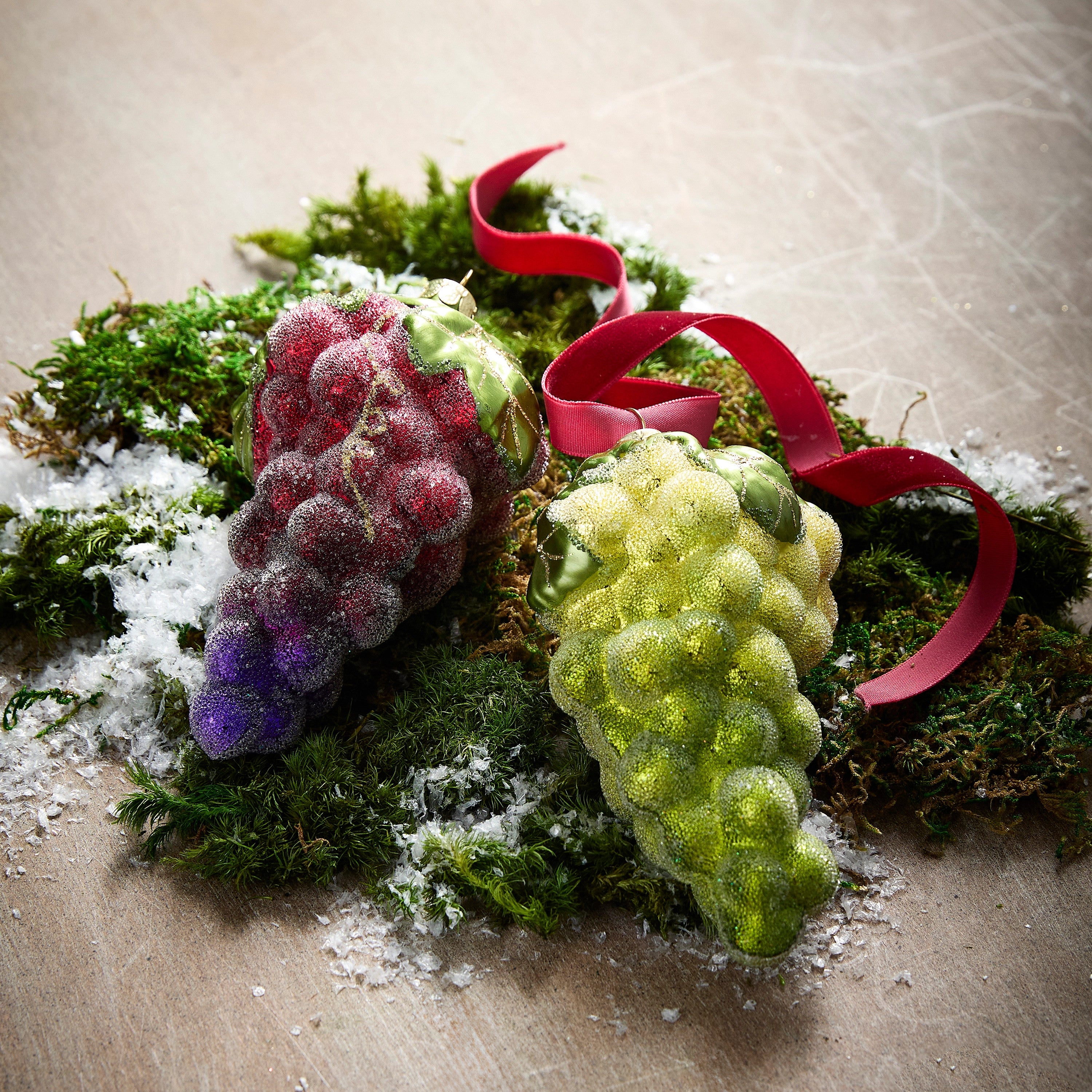 Red and green glittered glass grape cluster ornaments on moss with a red ribbon.