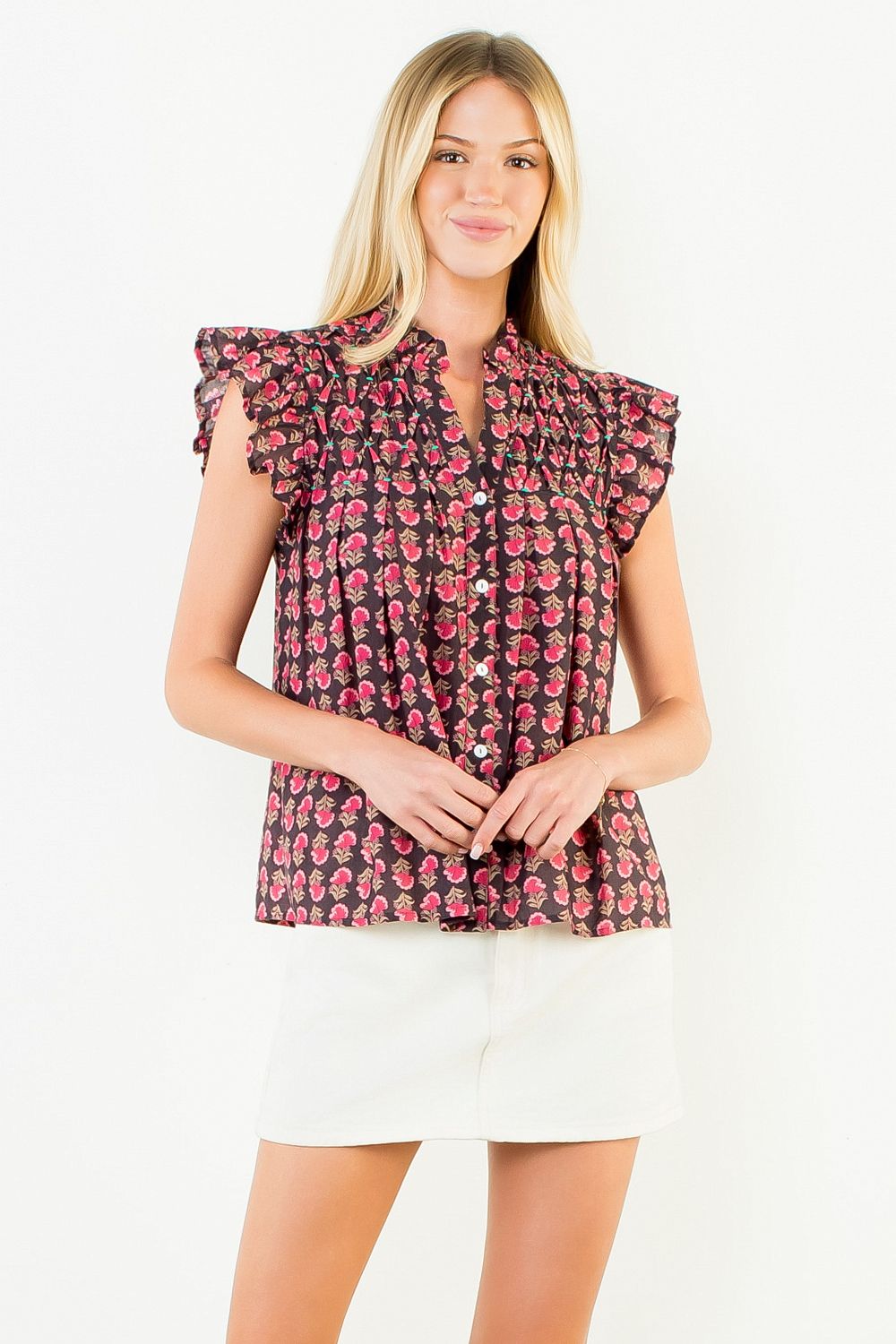 Woman wearing the Jane Flutter Sleeve Button Top in a dark floral print with white shorts.