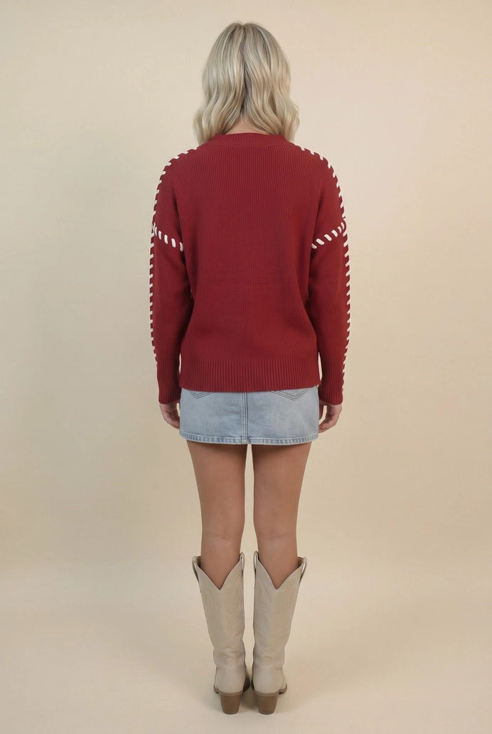 Back view of a woman wearing a red Oklahoma whip stitch sweater, denim skirt, and cream boots.