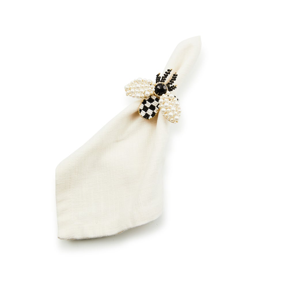 Bee napkin ring with pearl wings and a black and white checkered body on a white cloth napkin.