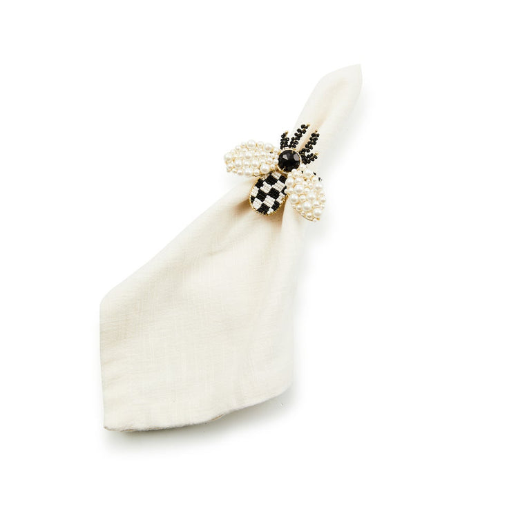 Bee napkin ring with pearl wings and a black and white checkered body on a white cloth napkin.