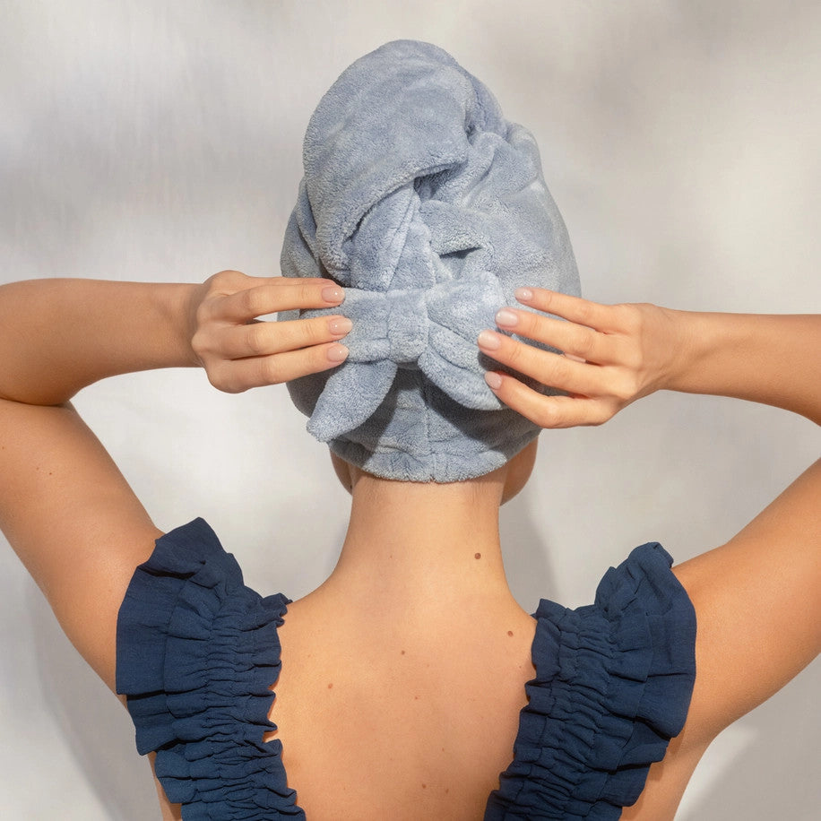 Back view of a person wearing a coastal blue plush microfiber hair towel turban with a bow detail.