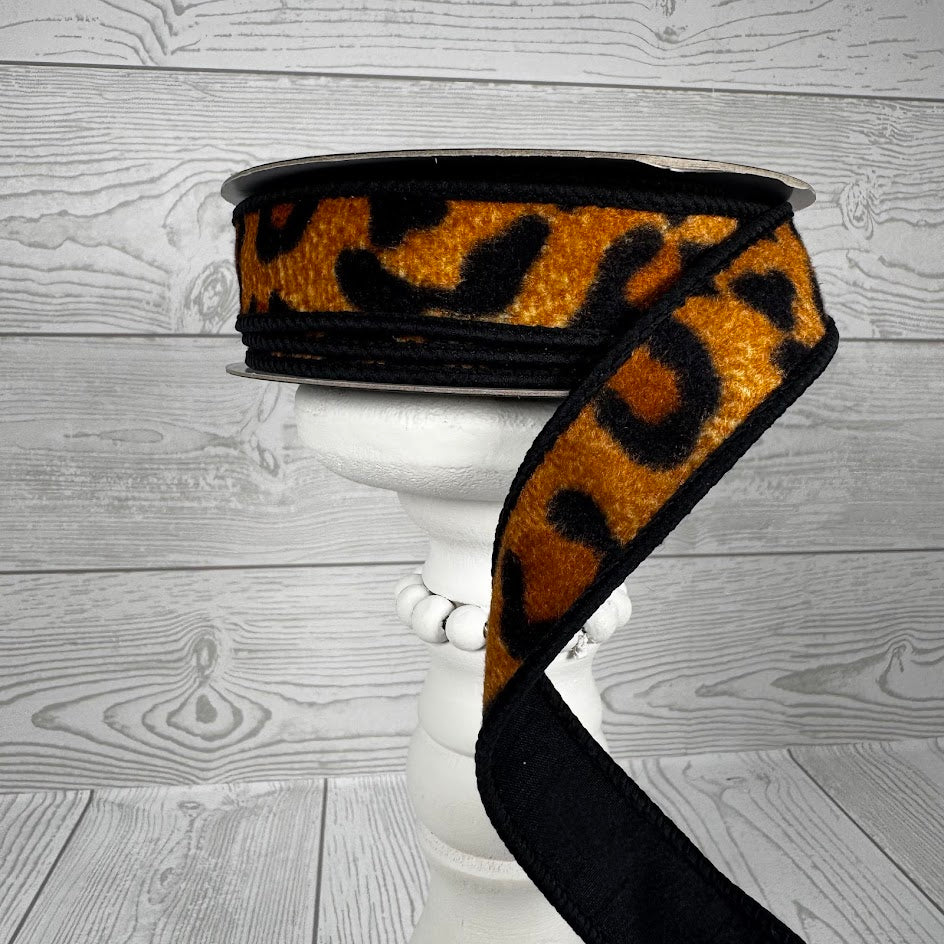 1 inch by 10 yard dupion fused leopard pattern ribbon on a spool over a white pedestal.