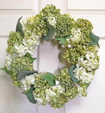 Round hydrangea wreath in soft pink flowers with green foliage on a natural branch base.