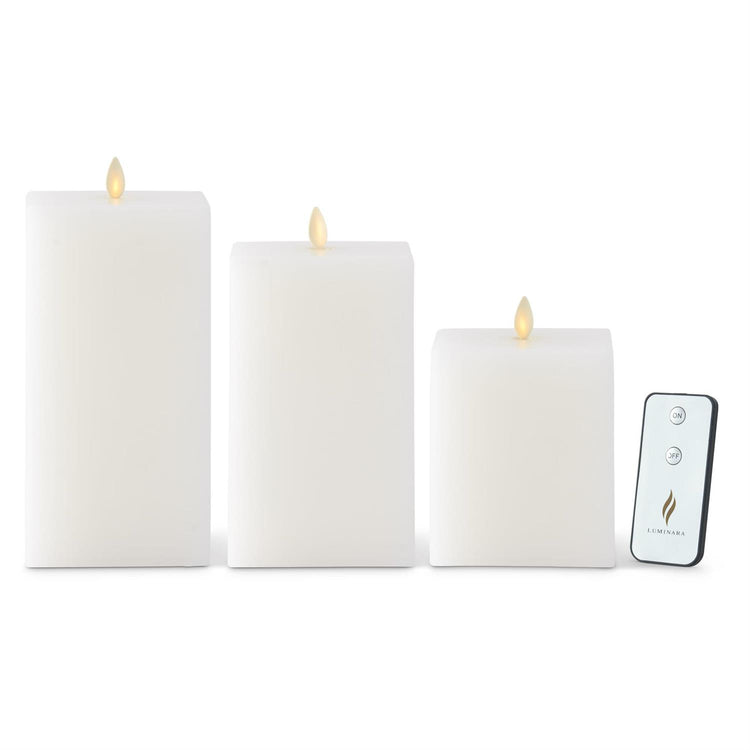 Three white square Luminara flameless wax candles in varying heights with a remote control.