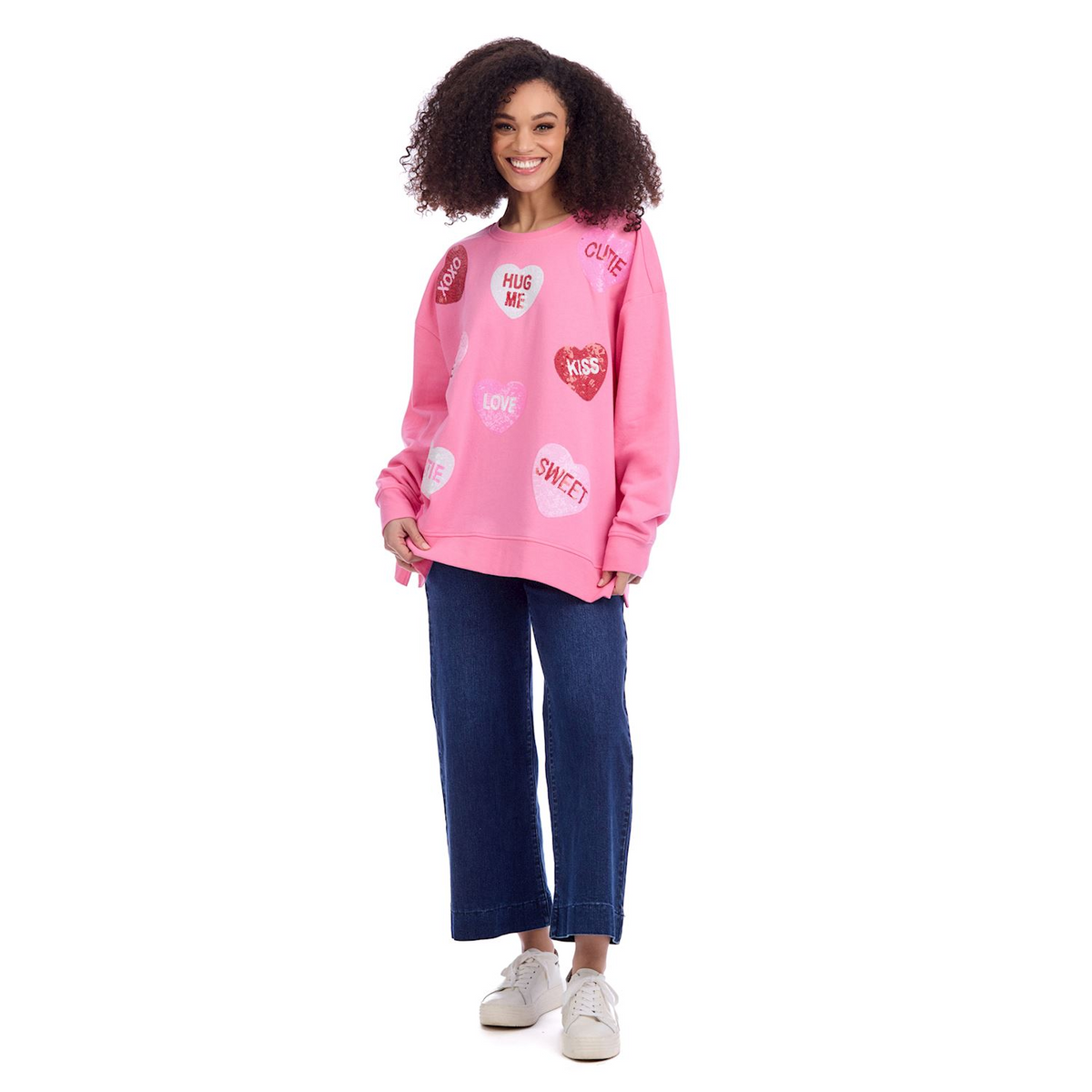 Woman wearing a pink oversized sweatshirt with sparkly heart graphics and wide-leg blue jeans.