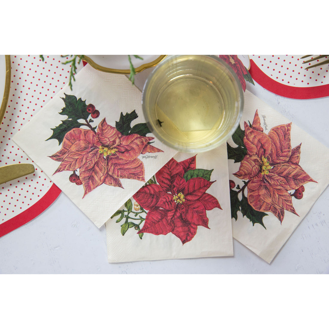 Red poinsettia floral cocktail napkin with green leaves on white background
