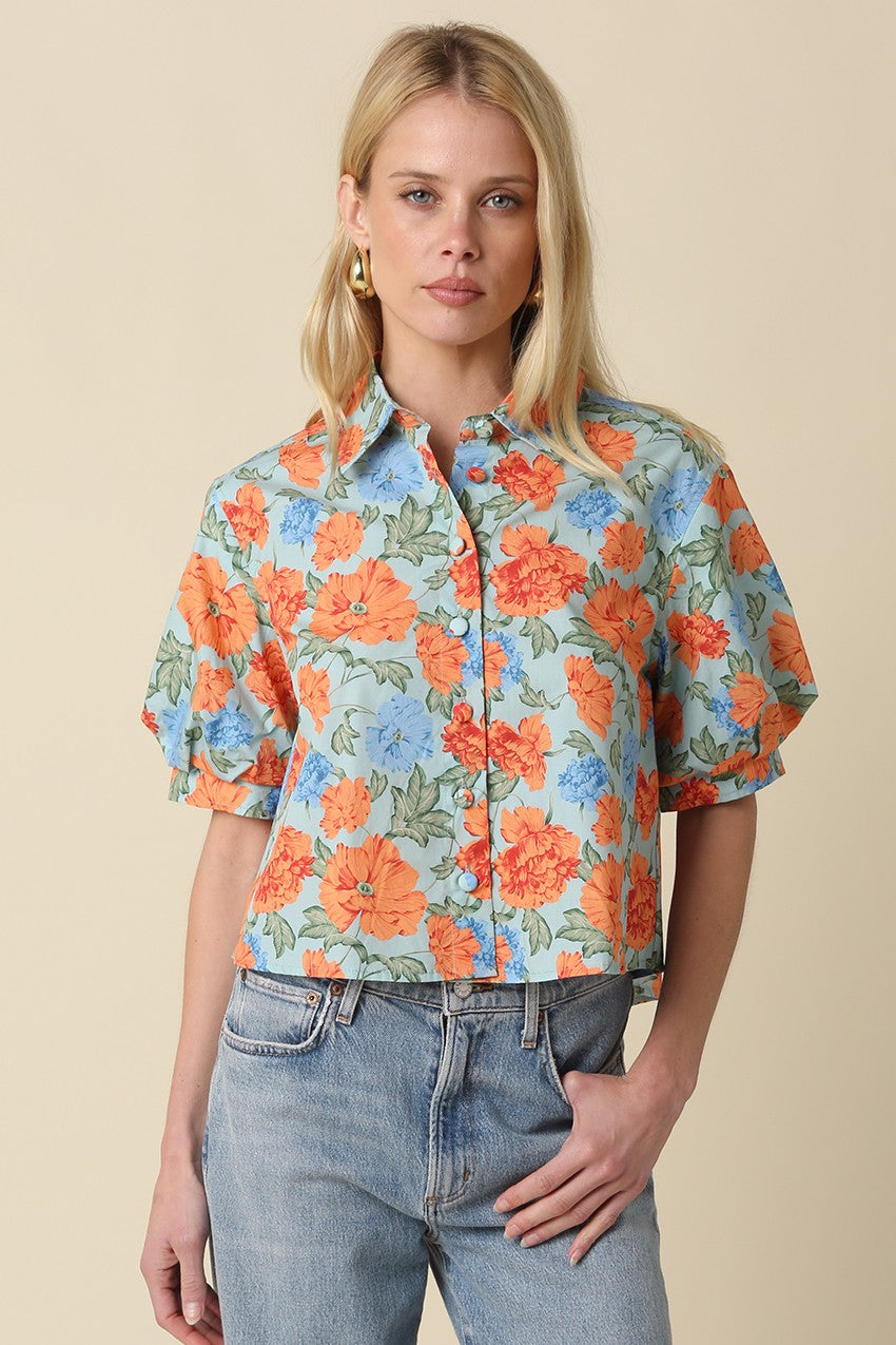 Woman wearing a light blue Mollie floral button-up top with orange flowers and puff sleeves.