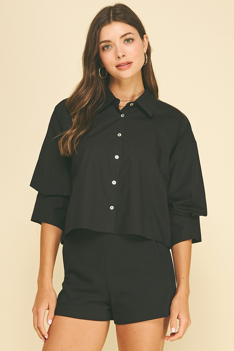 Woman wearing a black cropped button-down shirt with 3/4 tuck detailed sleeves and matching shorts.