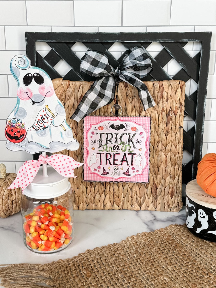 Mini pink Trick or Treat square print with a scalloped edge, hanging on a woven mat with a bow.