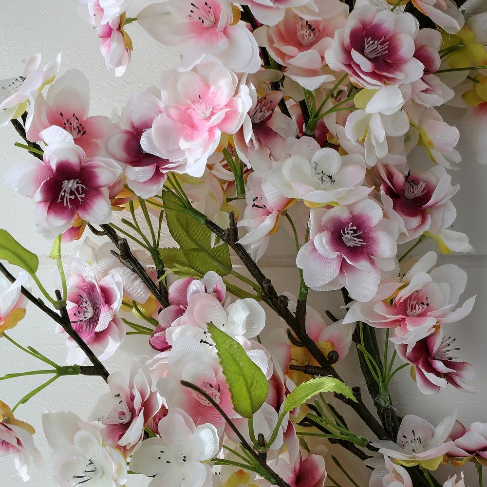 A round plastic wreath featuring soft pink cherry blossom flowers intertwined with green foliage.