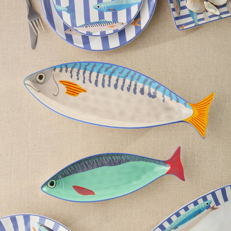 Two sculpted ceramic fish-shaped platters in blue, yellow, and green on a tan linen surface.