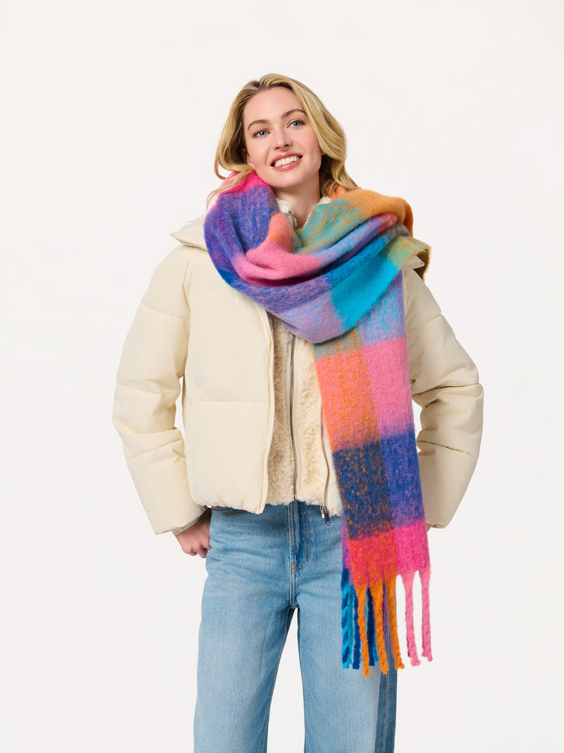 Woman wearing the Rola Scarf, an oversized multi-colored plaid scarf with fringe in vibrant shades.