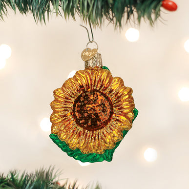 Glittery glass sunflower Christmas ornament hanging on a tree branch with bokeh lights.
