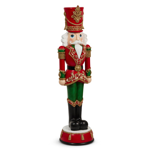 Red and green resin nutcracker figurine with gold accents and black boots on a decorative base.