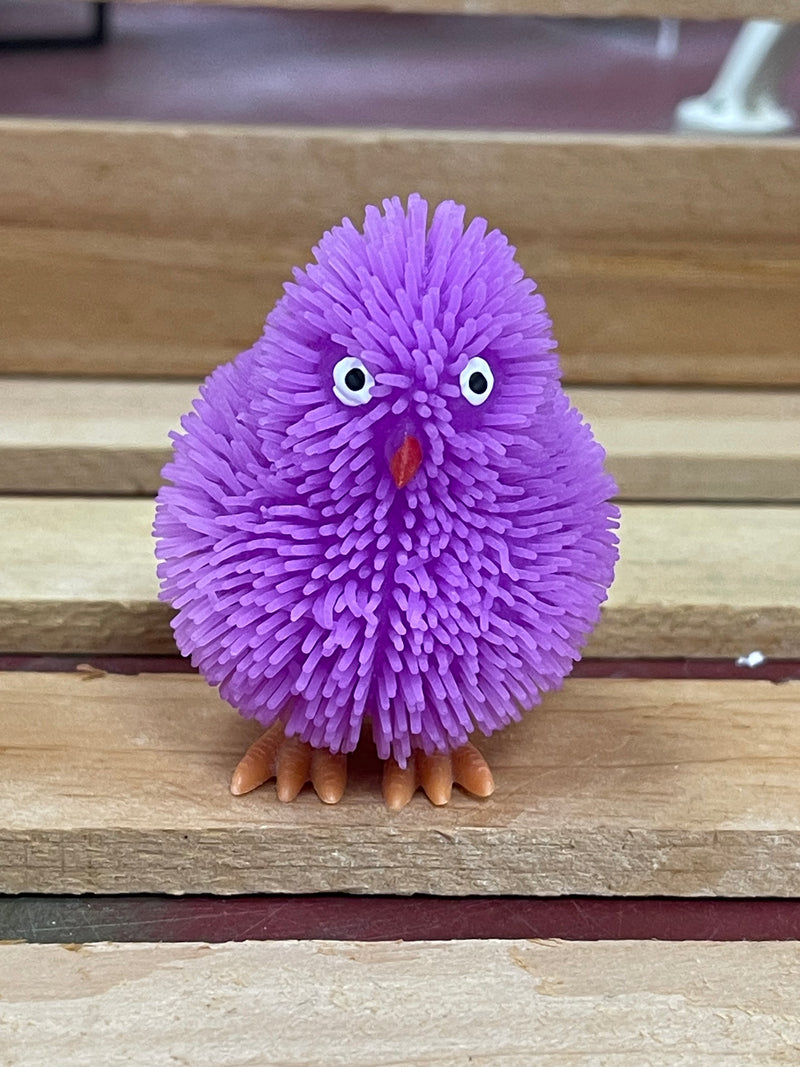 Purple fuzzy light-up chick toy with googly eyes and orange feet on a wooden surface.