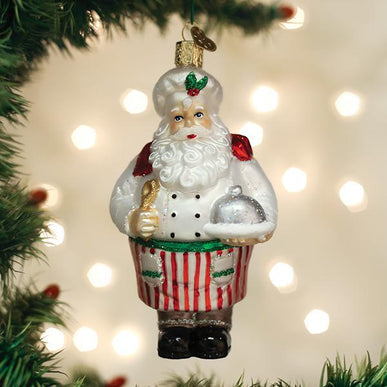 Chef Santa glass ornament wearing a white chef's hat, red striped apron, and holding a silver platter.
