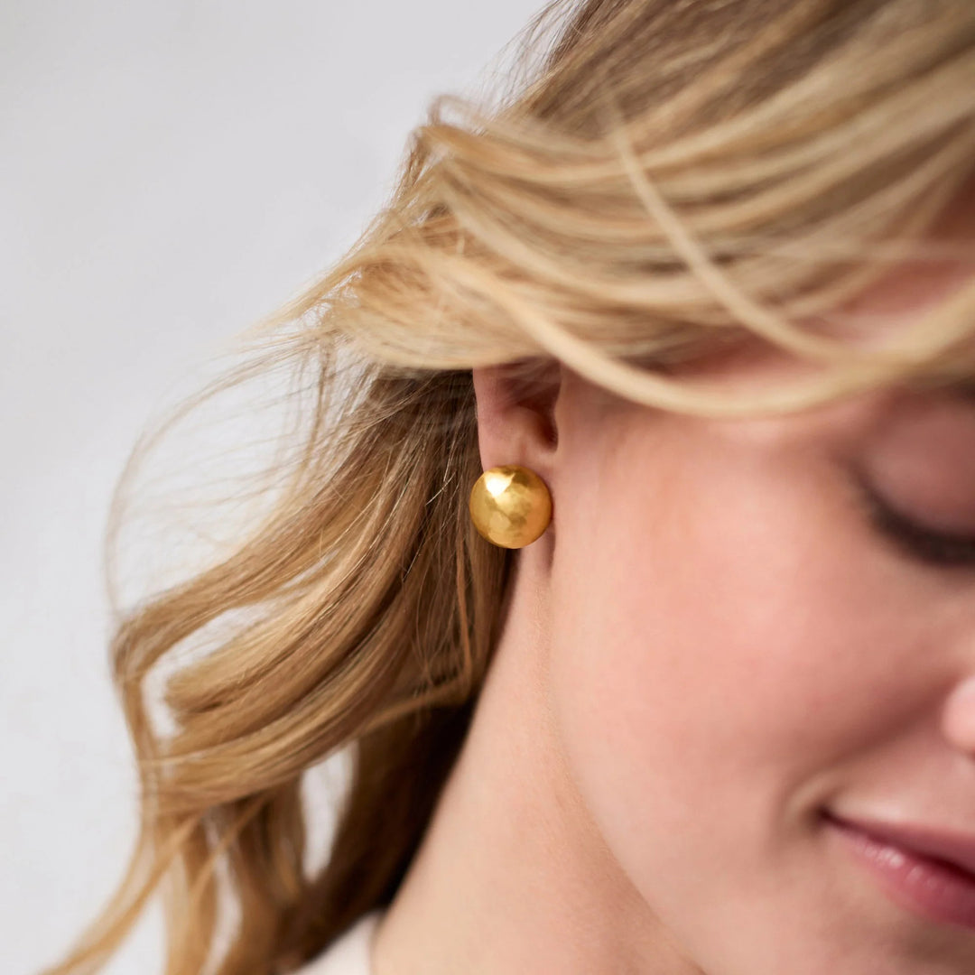 Close-up of a person wearing a Solara Stud Gold earring, a round 24K gold-plated hammered stud.