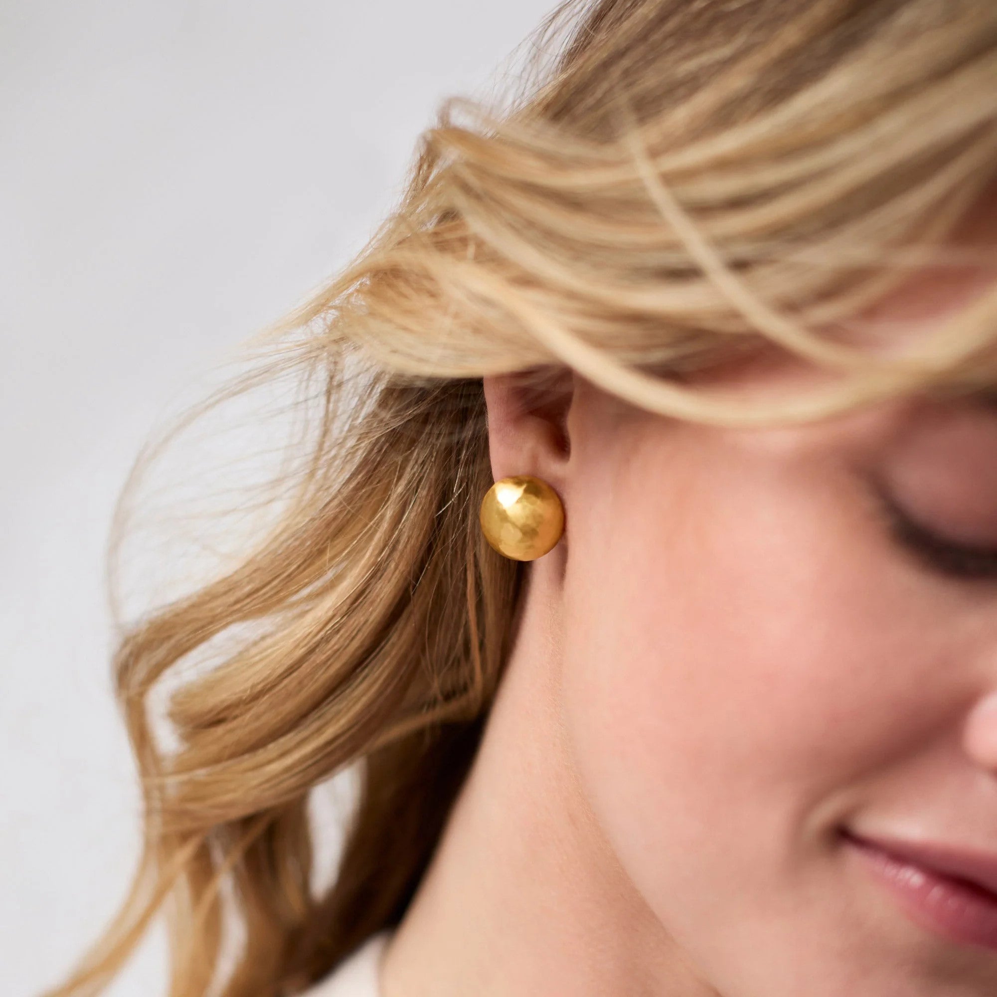 Close-up of a person wearing a Solara Stud Gold earring, a round 24K gold-plated hammered stud.
