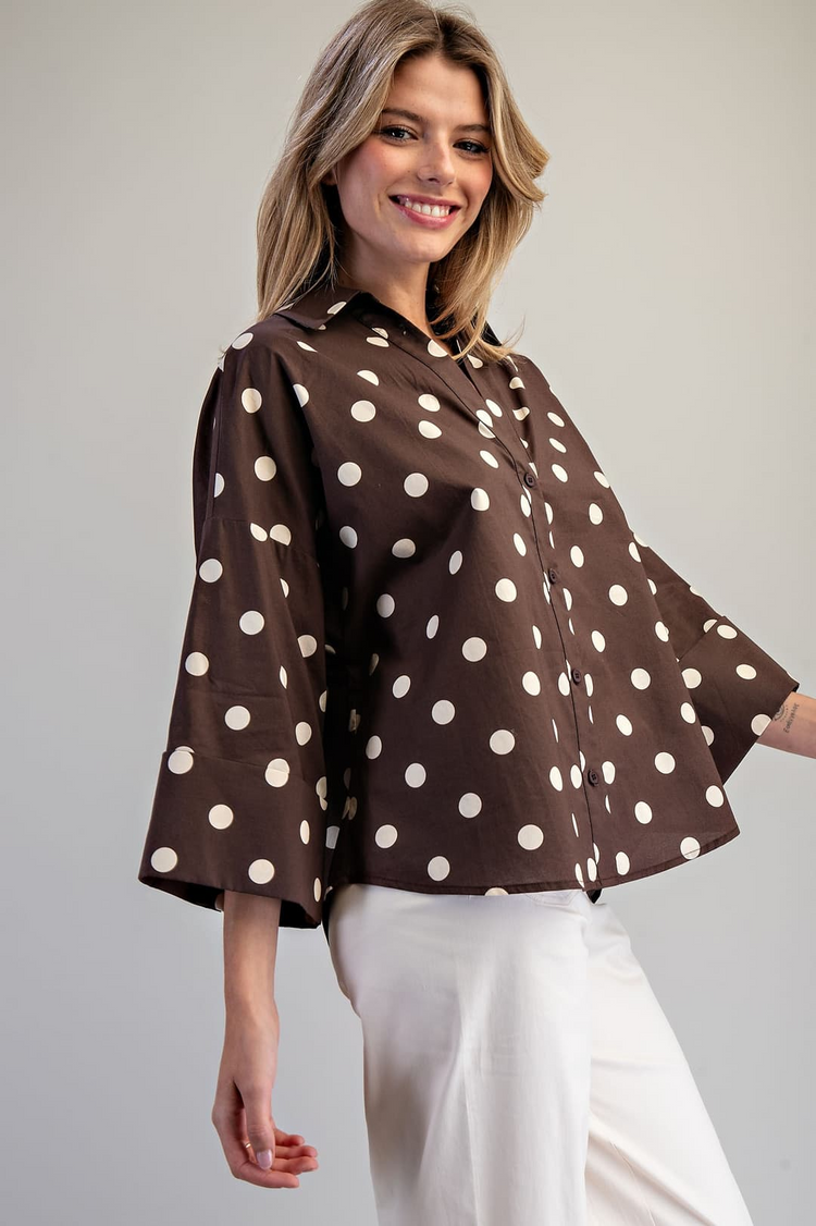 Woman wearing a brown Eliana Button Down Polka Dot Blouse with wide sleeves and white pants.