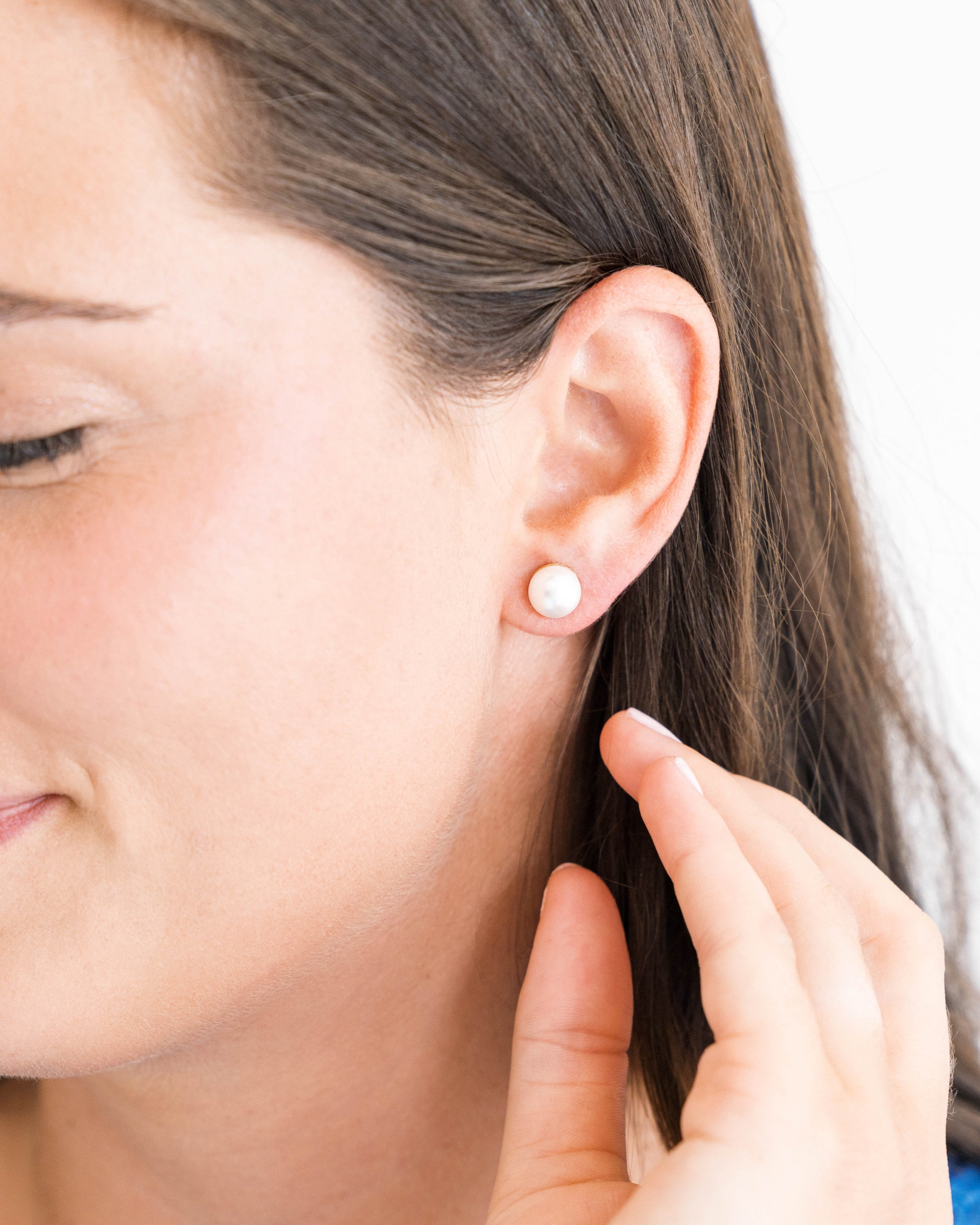 A woman wearing a classic white shell pearl stud earring on her left ear.
